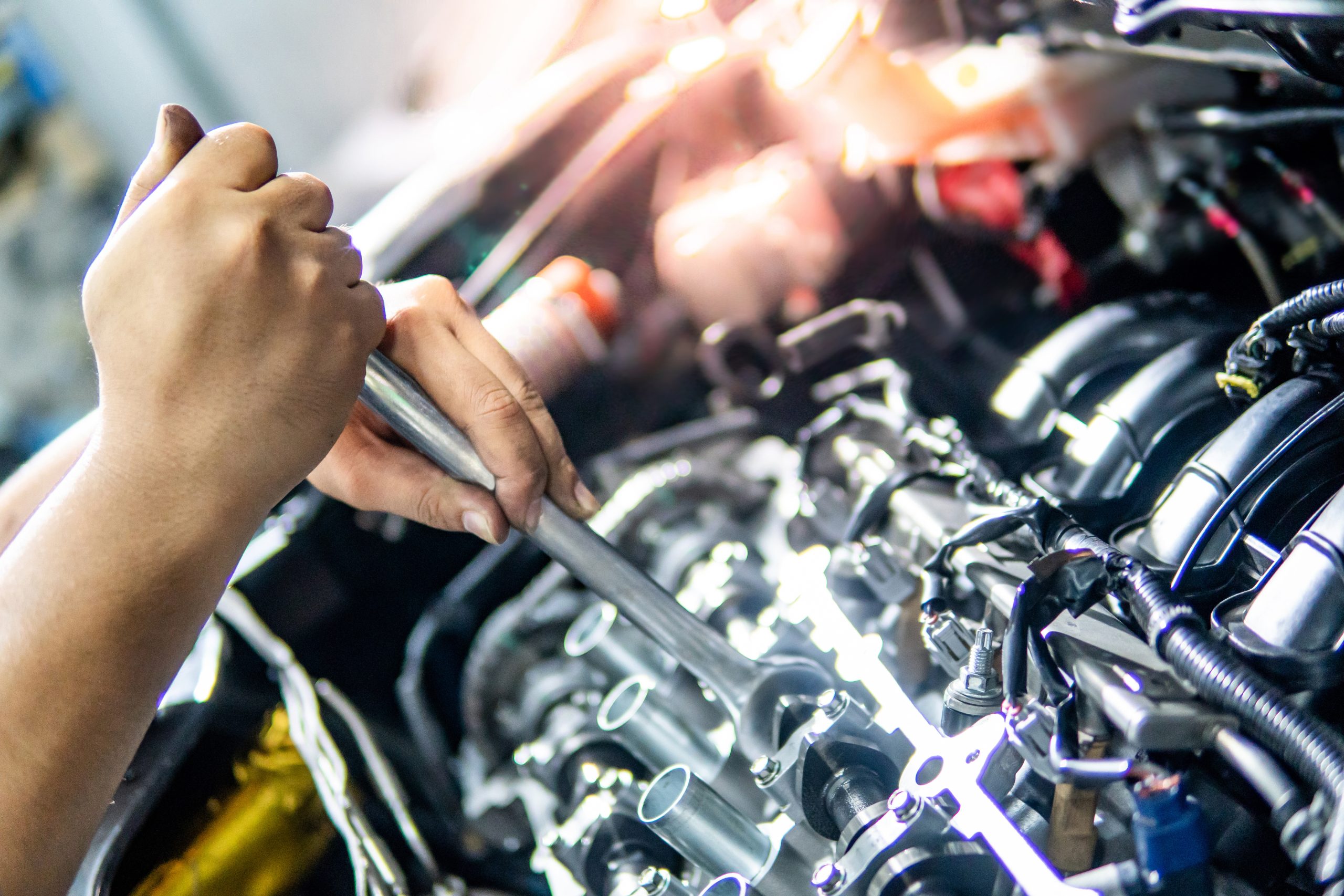 Male hand of auto mechanic fixing car engine with wrench in the garage. Automobile industry concept
